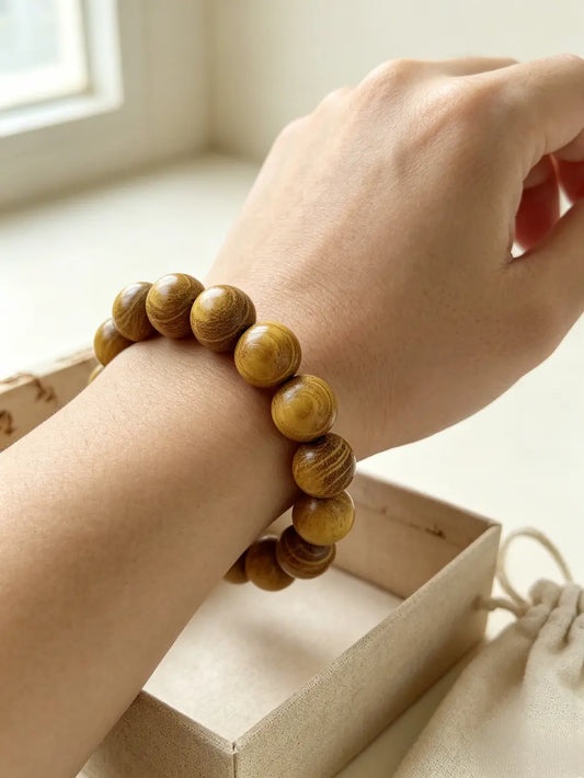  A wrist wearing a golden sandalwood bead bracelet, resting on a paper bag in soft daylight.