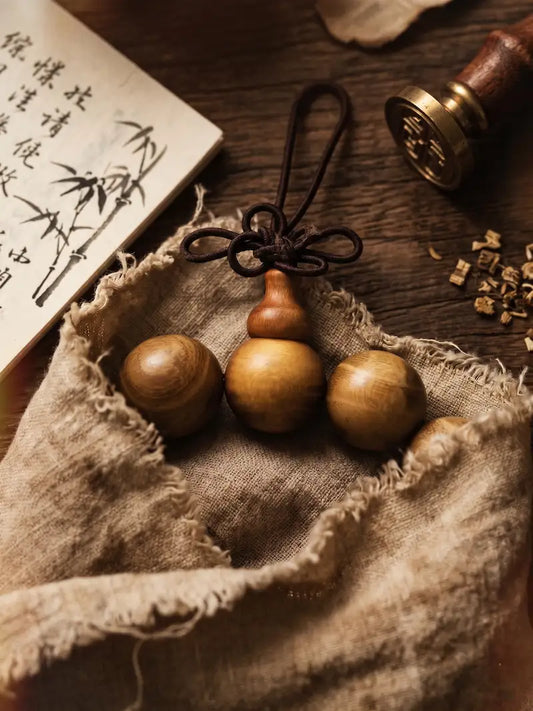 A golden sandalwood gourd knot bracelet resting on raw linen fabric, beside a bamboo ink painting book and a brass seal stamp — abundance as quiet presence, not display