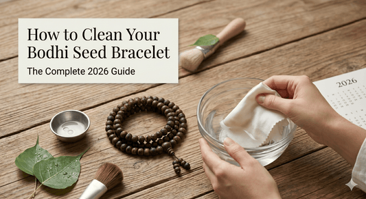 Hands cleaning a dark bodhi seed bracelet on a wooden table with a brush and small bowl.