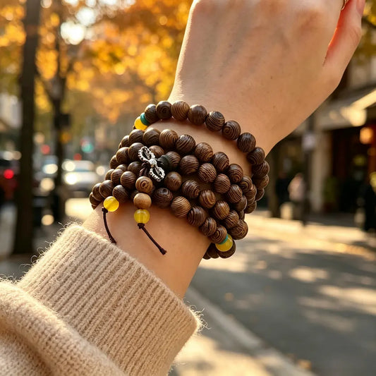 Close-up of a woman's wrist stacked with a 108-bead wenge wood mala bracelet and autumn knit sweater, warm golden-hour light.