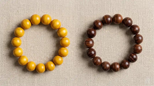 Two natural wood bead bracelets side by side on a beige linen background, contrasting a lighter golden-yellow wooden bracelet on the left with a darker chocolate-brown aged sandalwood bracelet with a rich natural patina gloss on the right.