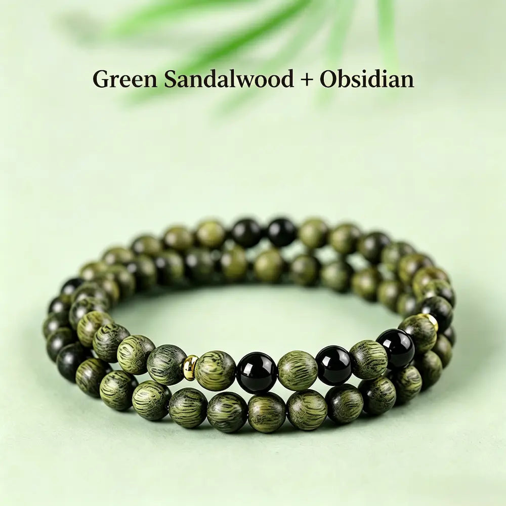 Double-wrap green sandalwood bracelet with three spaced black obsidian beads and brass spacers, on a light green surface.

