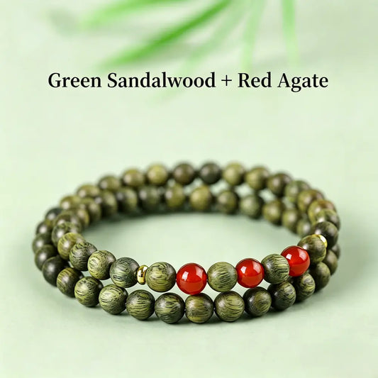 Double-wrap green sandalwood bracelet with three spaced red agate beads and brass spacers, on a light green surface.
