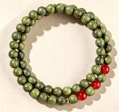Double-wrap green sandalwood bracelet with three spaced red agate beads and brass spacers, on a light green surface.