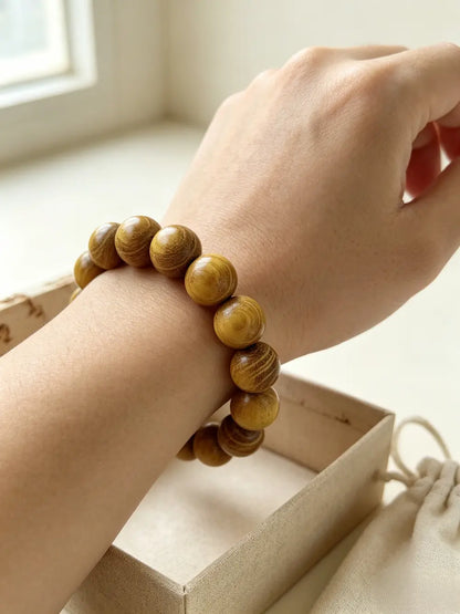 Close-up shot of golden sandalwood bracelet worn snugly on wrist, lightweight natural honey-toned wood with organic growth rings, adjustable elastic cord, minimalist meditation jewelry, thoughtful quiet gift for loved ones