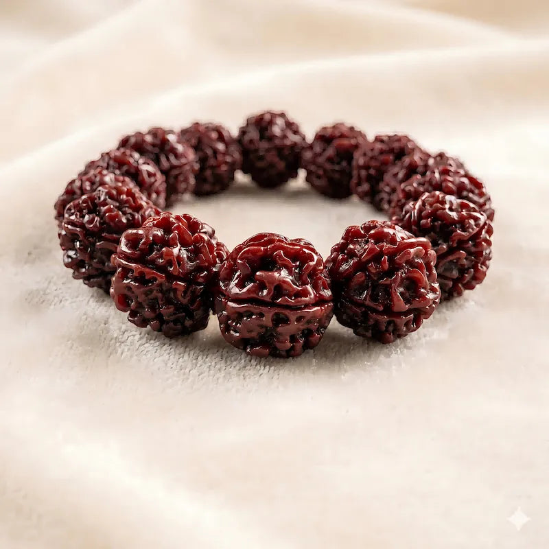 A premium six-faced jadeized rudraksha bead bracelet with a rich dark red glossy patina, resting elegantly on a soft beige fabric background.