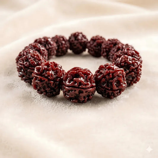 A premium six-faced jadeized rudraksha bead bracelet with a rich dark red glossy patina, resting elegantly on a soft beige fabric background.
