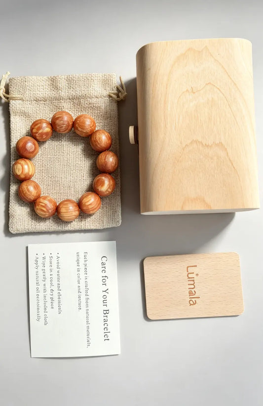 20mm Dragon Blood Wood bracelet laid on a cotton pouch next to Lumala's birch bark gift box and care card.