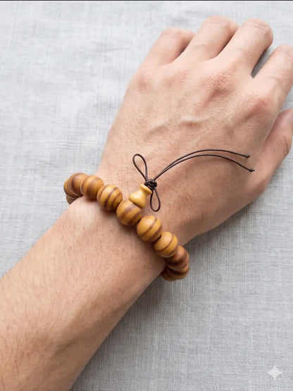 A close-up of a wrist wearing a handcrafted natural wood bead bracelet with an adjustable bow knot, illuminated by soft, bright natural sunlight against a serene gray fabric background.
