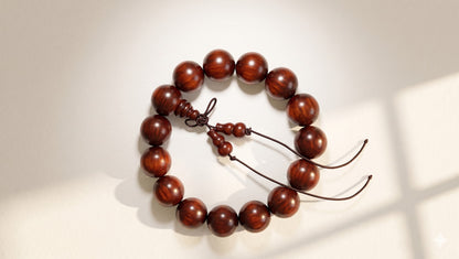 A handcrafted 15mm rhinoceros rosewood bracelet isolated on a bright, crisp white background with soft, natural light shadows accentuating the glossy wood texture.