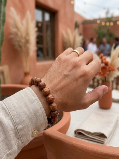 Rosewood bracelet on wrist with gold ring, terracotta garden wedding setting with pampas grass
