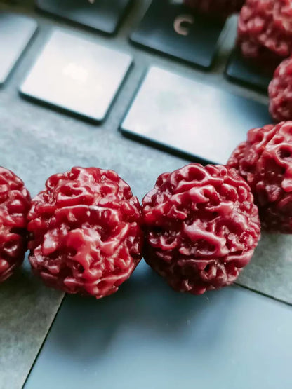 Macro detail shot of glossy red rudraksha meditation beads placed horizontally over a dark mechanical computer keyboard.