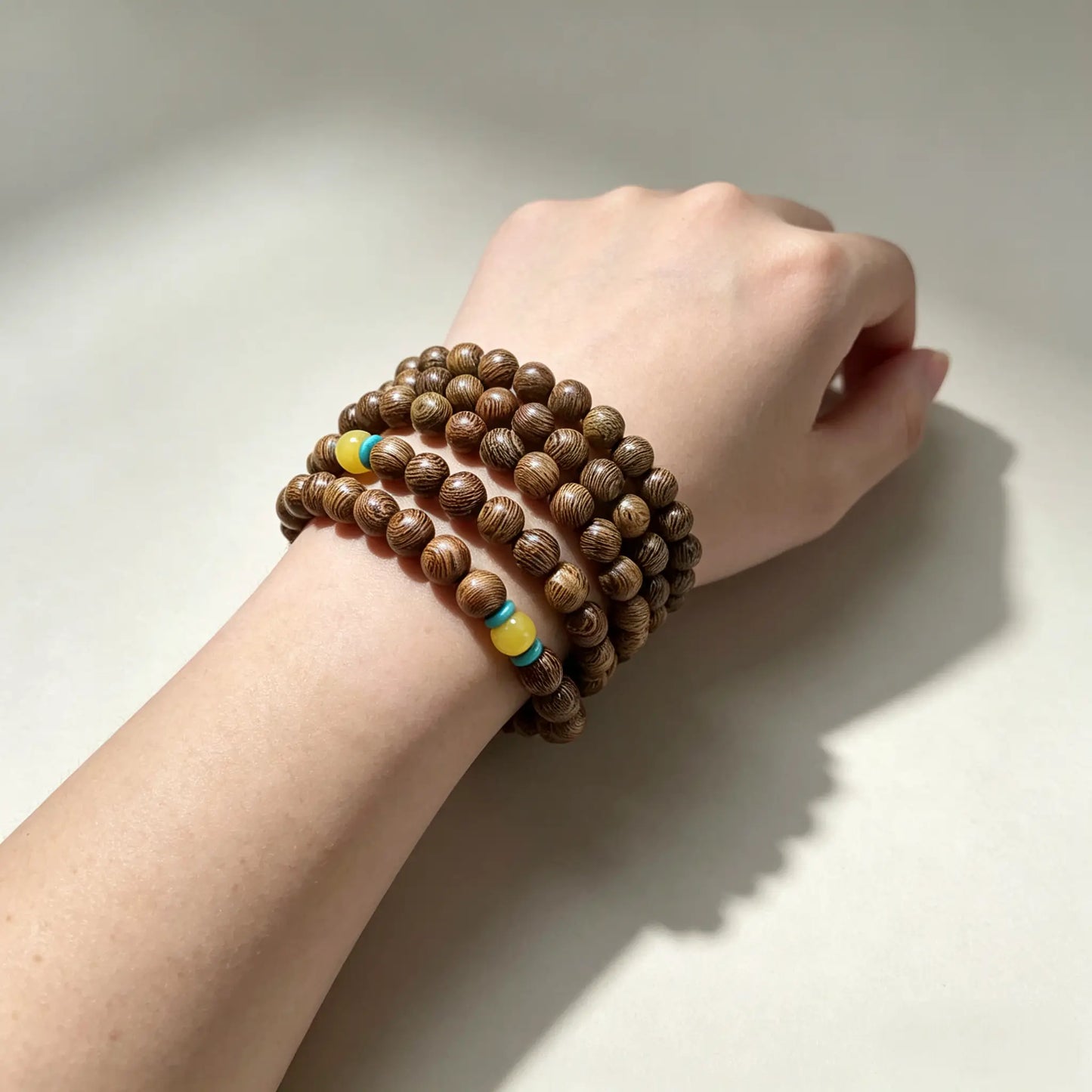 Detailed shot of a 108-bead wenge wood mala bracelet wrapped around a woman's wrist, showing dark feather grain and turquoise spacer beads.
