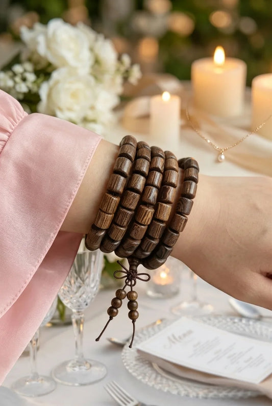 Boho wedding lifestyle photo, wenge wood mala bracelet on bride’s wrist, wedding reception table with white roses and candlelight, spiritual gifting mala strand